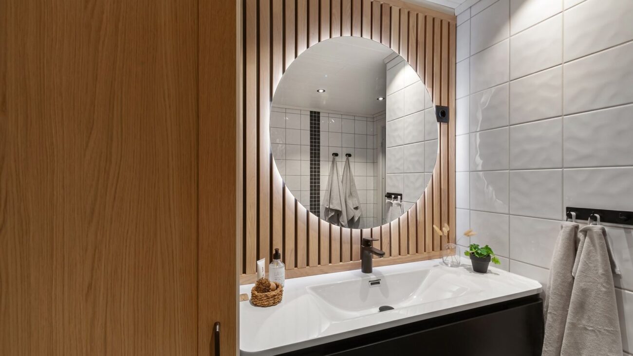 Lavabo com espelho arredondado, madeira ripada e iluminação suave em composição acolhedora