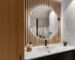 Lavabo com espelho arredondado, madeira ripada e iluminação suave em composição acolhedora