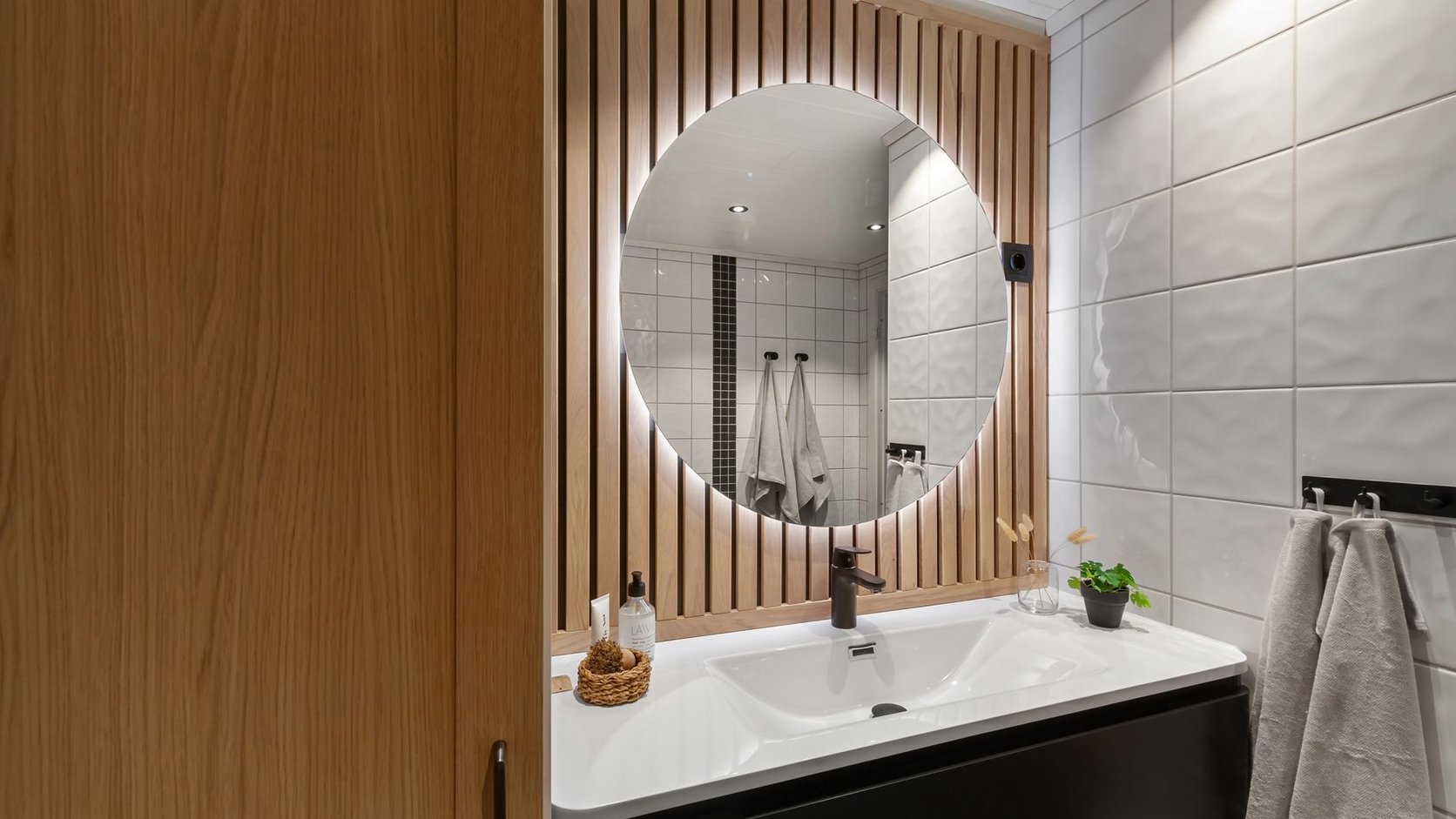 Lavabo com espelho arredondado, madeira ripada e iluminação suave em composição acolhedora