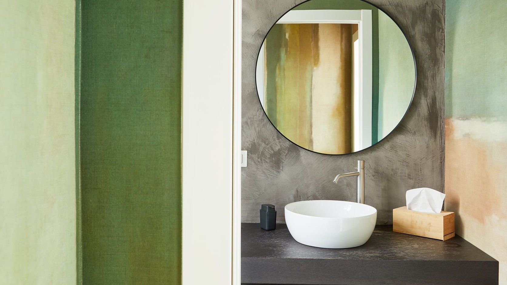 Lavabo pequeno com espelho arredondado, bancada escura e composição visual leve